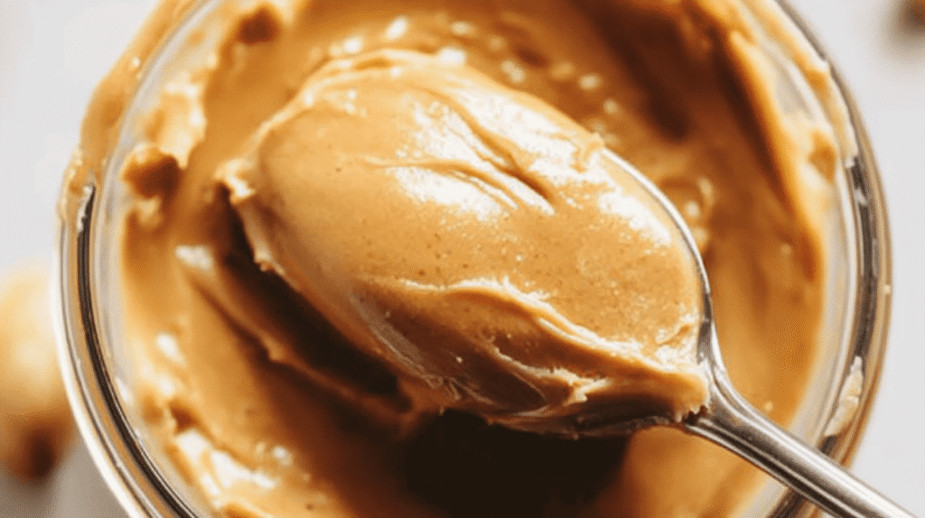 A close-up of a spoonful of creamy peanut butter from a glass jar.