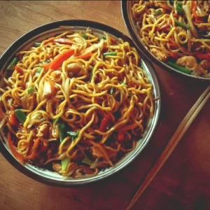 A plate of savory fried noodles topped with vegetables and sauce