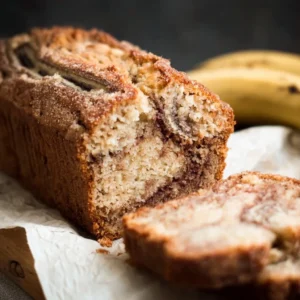 Loaf of cinnamon swirl banana bread with a slice taken out, showcasing moist texture.